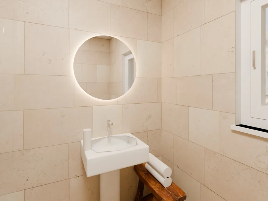 Render del bagno con lavabo a colonna, specchio tondo illuminato e rivestimento in pietra chiara